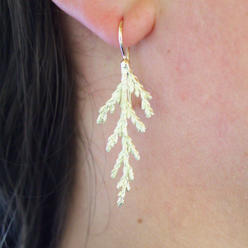 Gouden oorhaken met het patroon van een cedertak design en handgemaakt door Goudsmederij Goedbloed op model