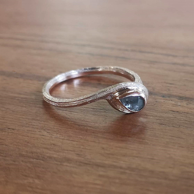 Goud en golvend bamboe eindigend in een loop waarin een roosgeslepen natuurlijk grijze diamant is gezet. Een asymmetrisch organische elegante solitaire ring.