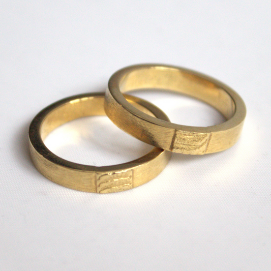 Klassieke trouwringen met een zandgegoten imprint van de zee als tussenstuk minimalistisch handgemaakt door Goudsmederij Goedbloed