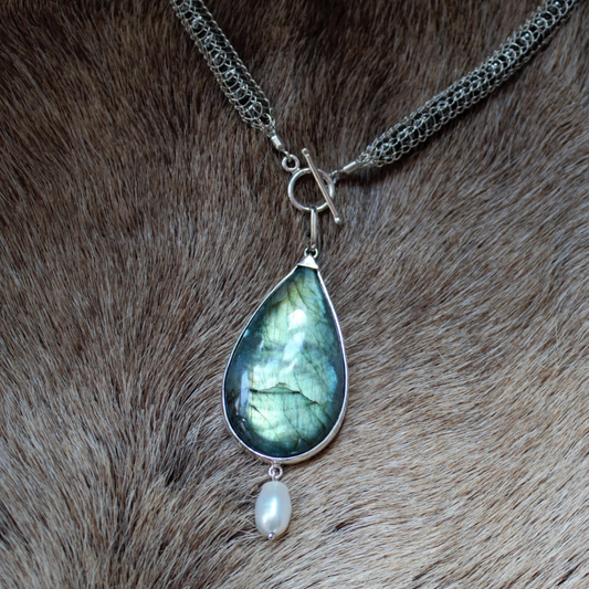 Van zilverdraad handgeweven collier opgevuld met hematiet en een hanger met een peervormige Labradoriet waaronder speels een witte barokparel hangt. Handgemaakt volgens oude smeedtechnieken door Goudsmederij Goedbloed