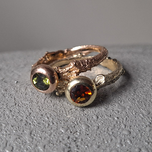 Handgemaakt gouden solitaire ringen in 14 karaat geel en roodgoud met diverse kleuren edelstenen gezet in een ronde volle zetkast en met een natuurlijke taktextuur in de ringband. Ontwerp en uitvoering door Goudsmederij Goedbloed