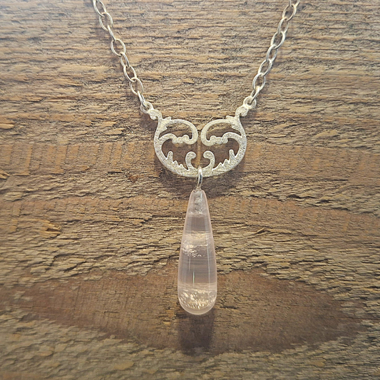 Zilver 925 ankerketting met een symmetrische tussenhanger met krulwerk en op het balanspunt een ophanging met een unieke druppelvormige rozenkwarts. Handgemaakt ontwerp door Goudsmederij Goedbloed